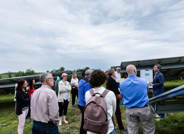 A group of people standing near solar panels in a field.