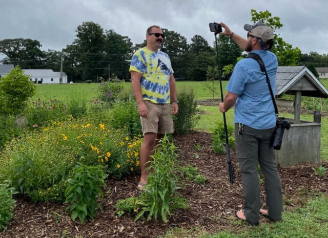 A person filming someone speaking in a garden