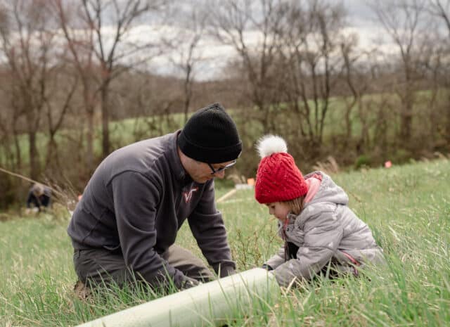 An adult and a child plant a tree in a field