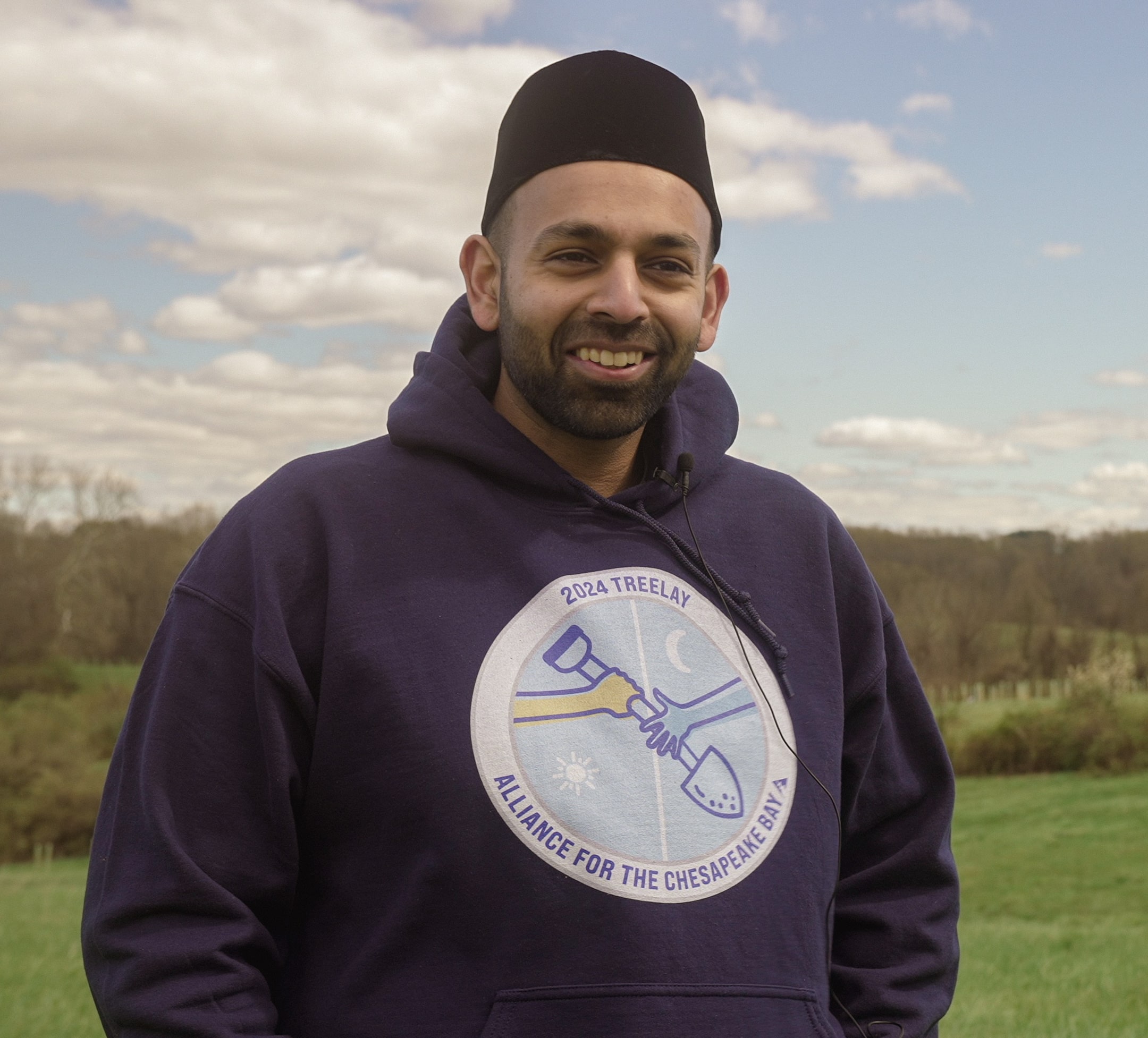 A person smiling for a photo in a field, wearing a Treelay sweatshirt