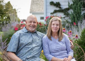 The Glatfelters smiling and sitting next to each other with a flowering garden backdrop. George Glatfelter has his arm around his wife.