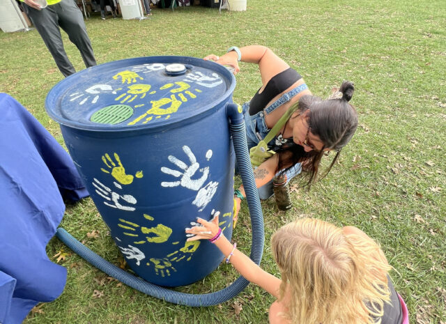 Two people kneeling and pressing one hand each to a rain barrel to imprint their handprint on the rain barrel.