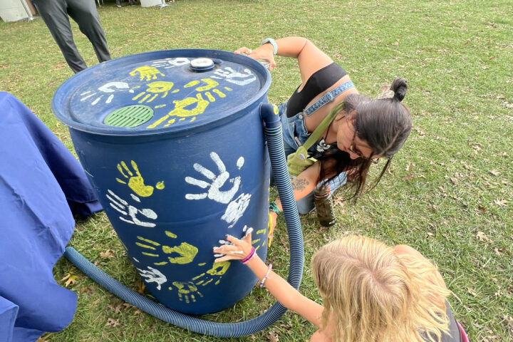 Two people kneeling and pressing one hand each to a rain barrel to imprint their handprint on the rain barrel.