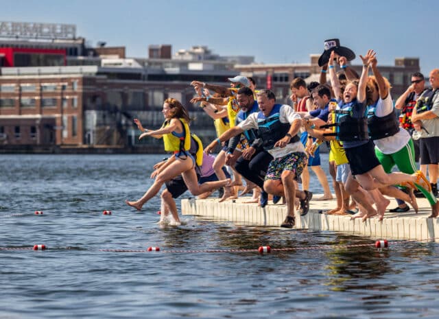 A group of people in floatation vest jump into the water off of a dock