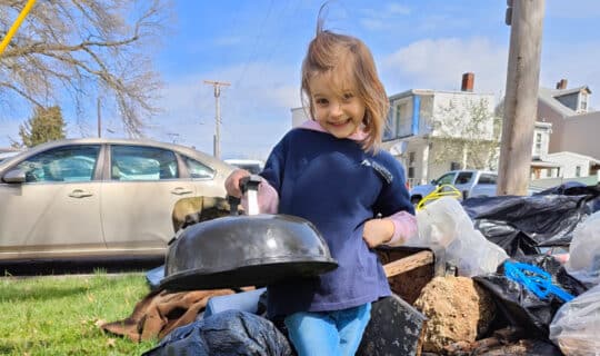 A young volunteer smiles and holds up a grill lid