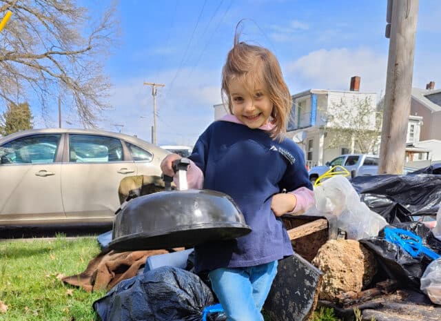 A young volunteer smiles and holds up a grill lid