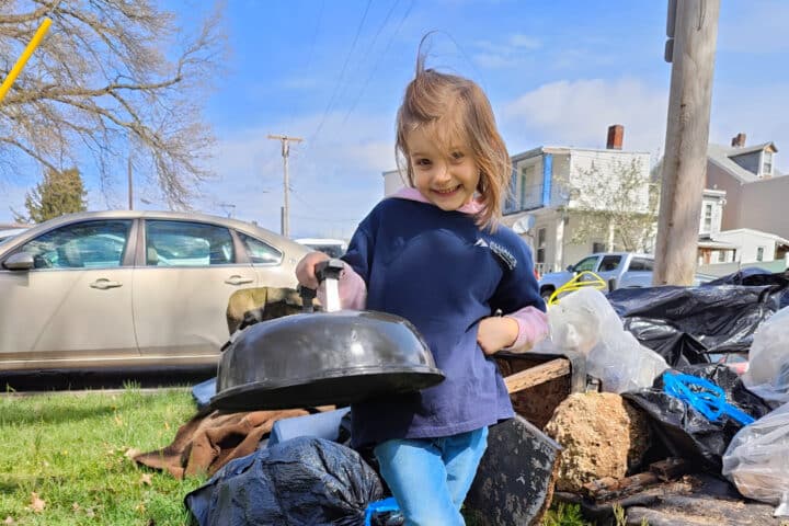 A young volunteer smiles and holds up a grill lid