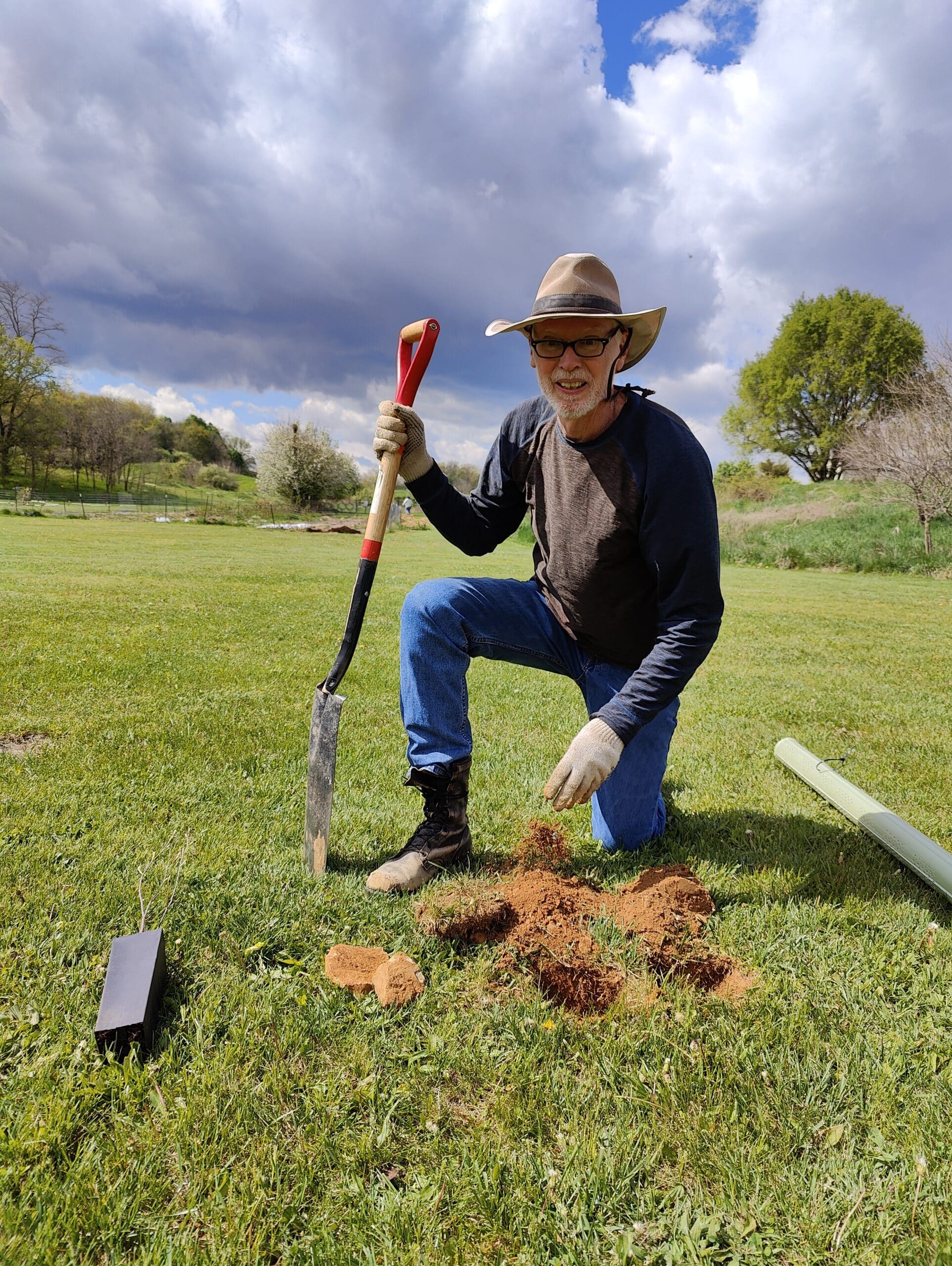 A person smiling in a field while preparing a hole to plant a tree in