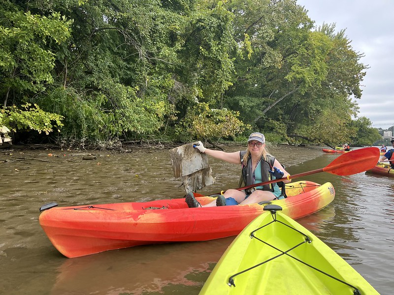 A volunteer in a red kayak holds up a large piece of soggy cardboard pulled out from the Anacostia River.