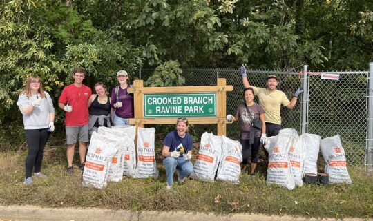 A group of volunteers pose in front of the Crooked Branch Ravine Park sign with their trash bags.