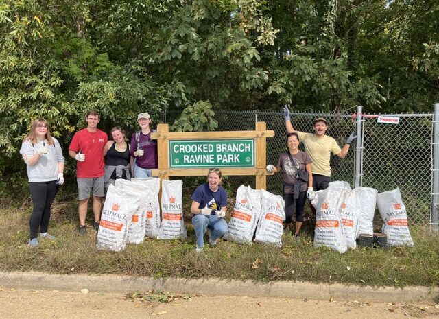 A group of volunteers pose in front of the Crooked Branch Ravine Park sign with their trash bags.