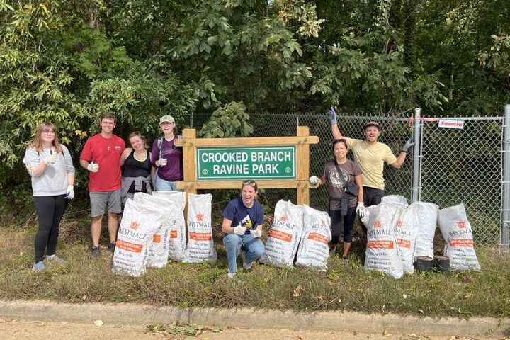 A group of volunteers pose in front of the Crooked Branch Ravine Park sign with their trash bags.