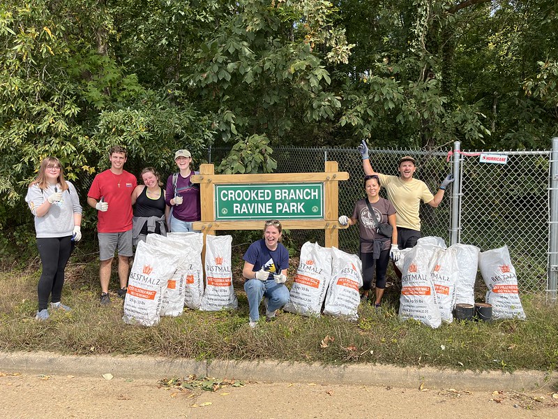 A group of volunteers pose in front of the Crooked Branch Ravine Park sign with their trash bags.