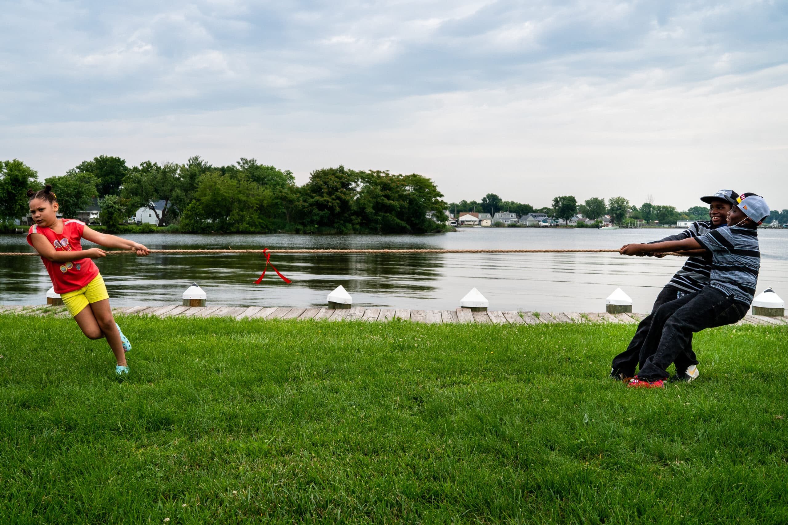 Young people playing a game of tug of war next to a body of water