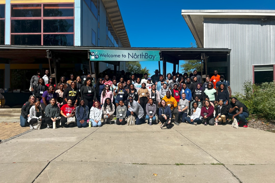 A group of people pose for a photo on a sunny day in front of a large building