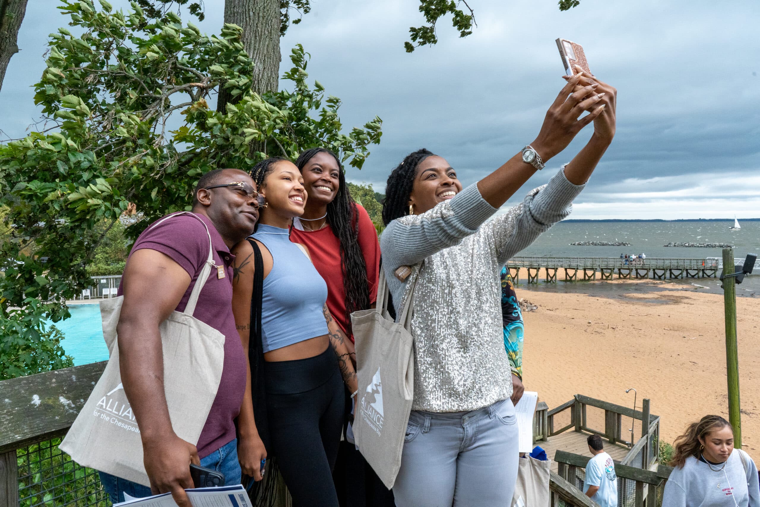 A group of people smile while one person takes a selfie with their phone