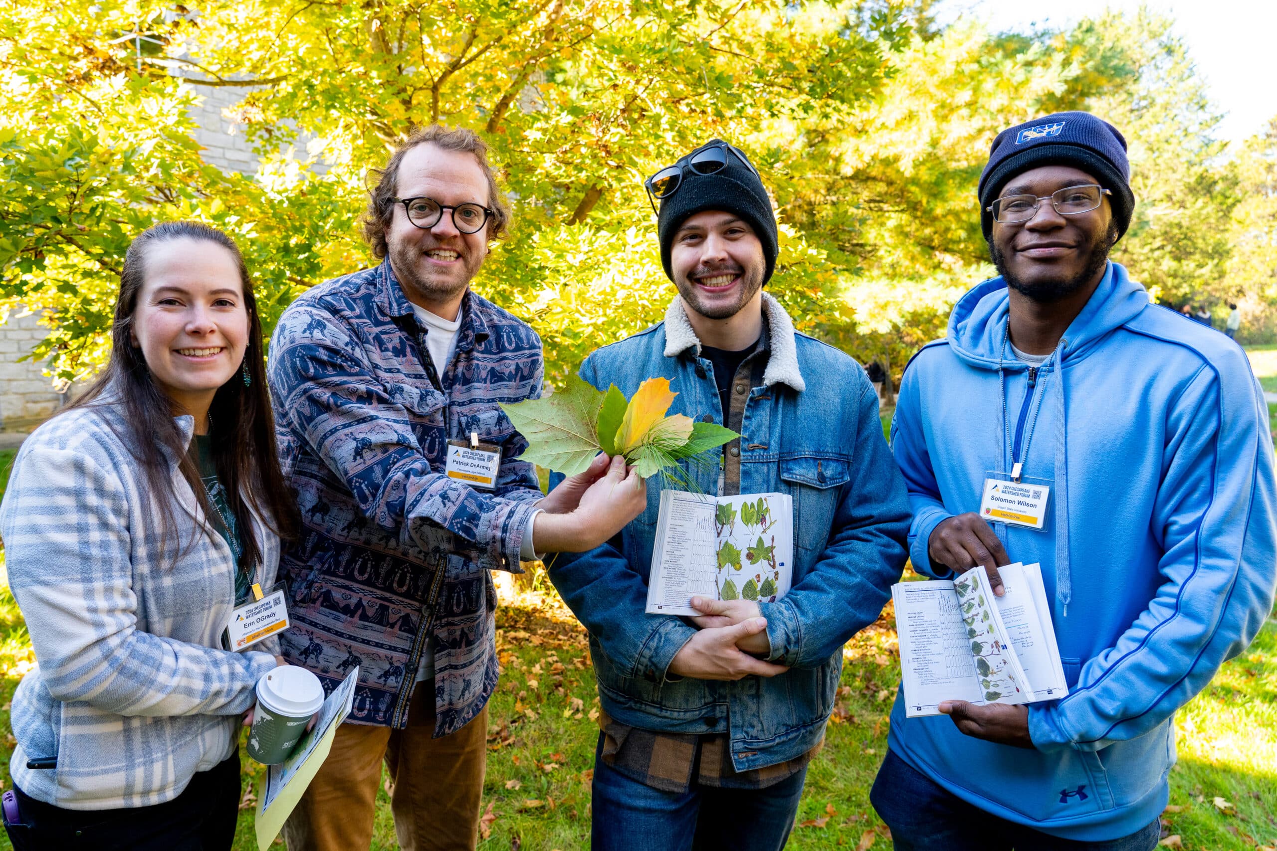 People smiling and holding up different leaves and tree identification books