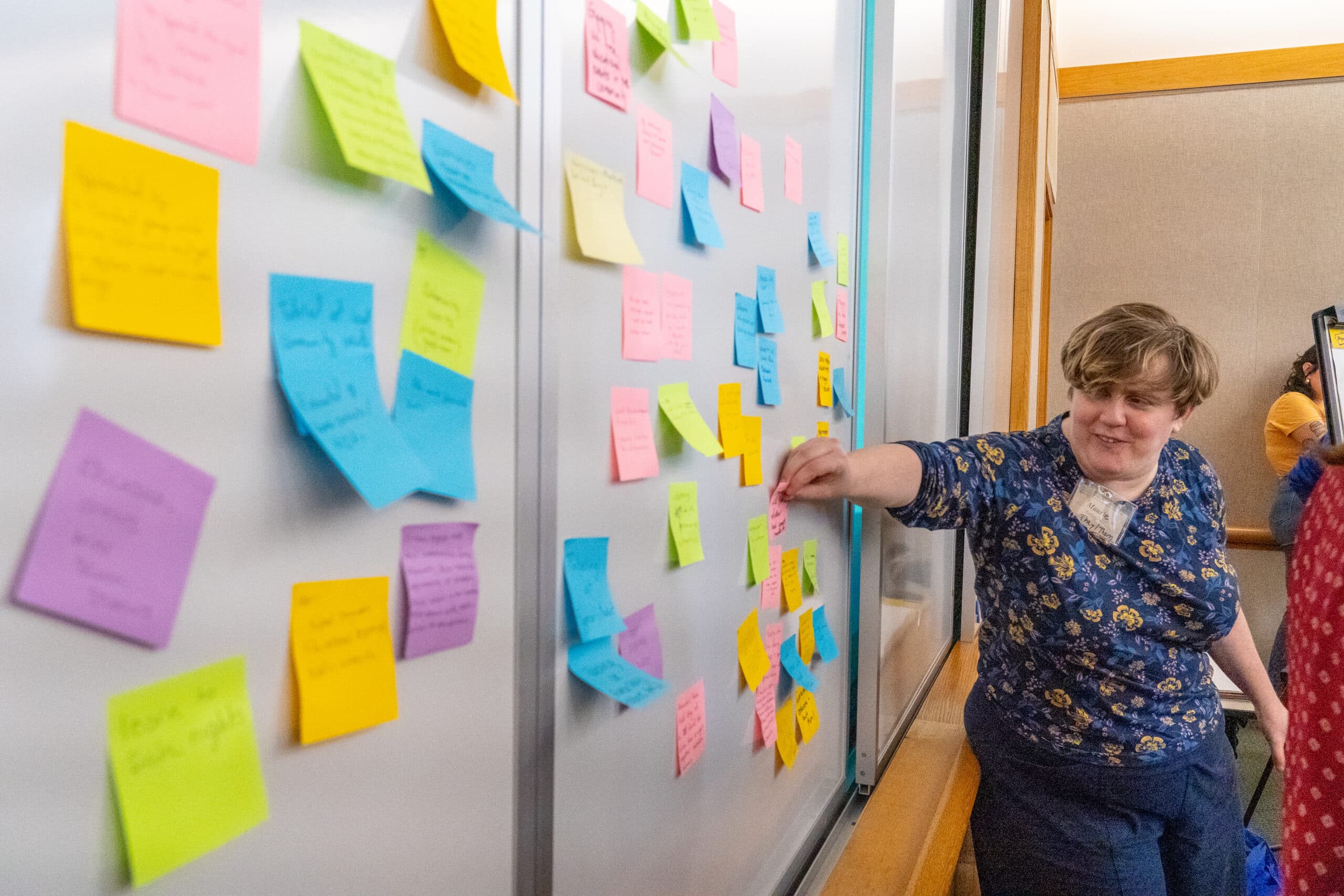 A person sticking a post it note onto a white board