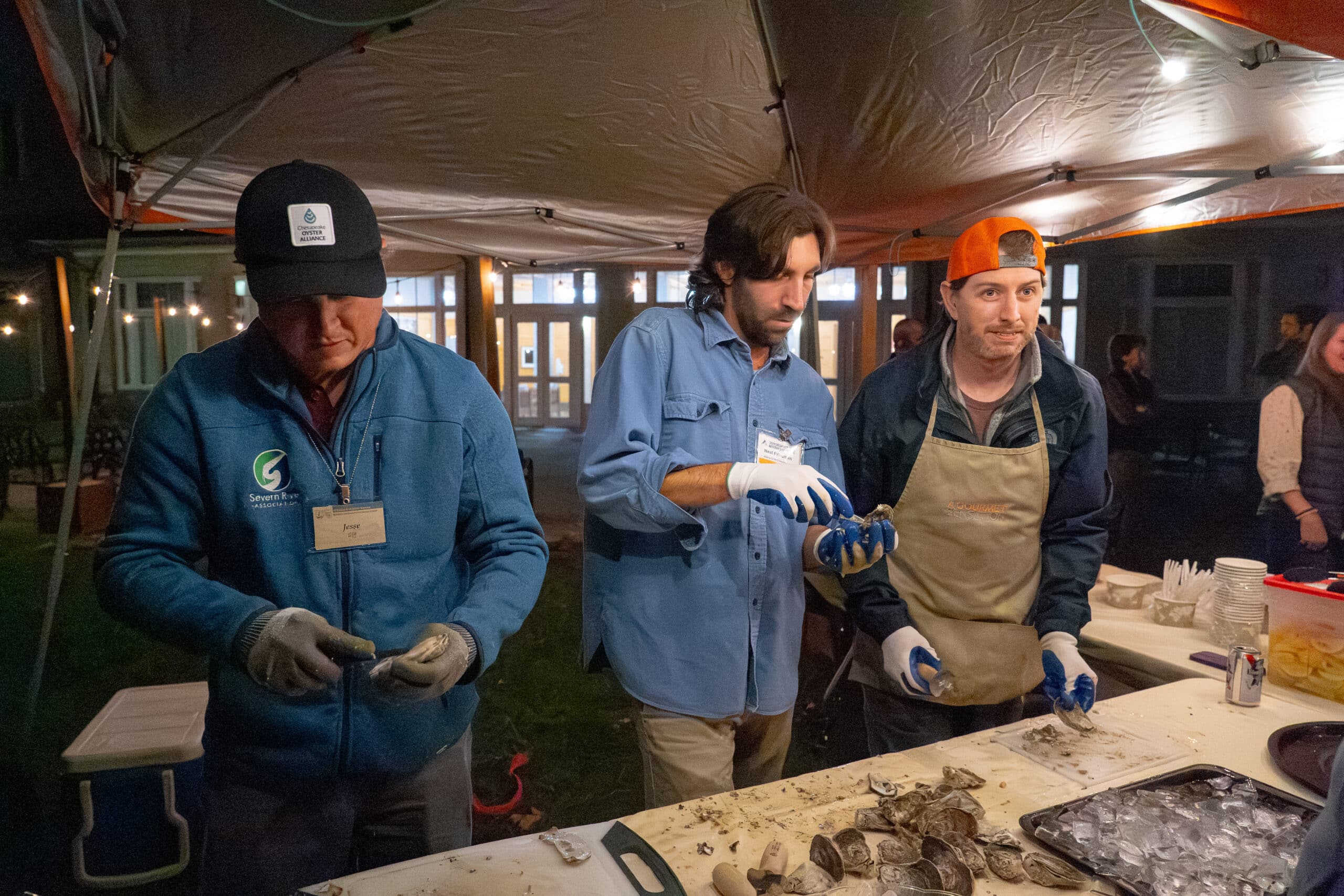 Three people shucking oysters under a canopy