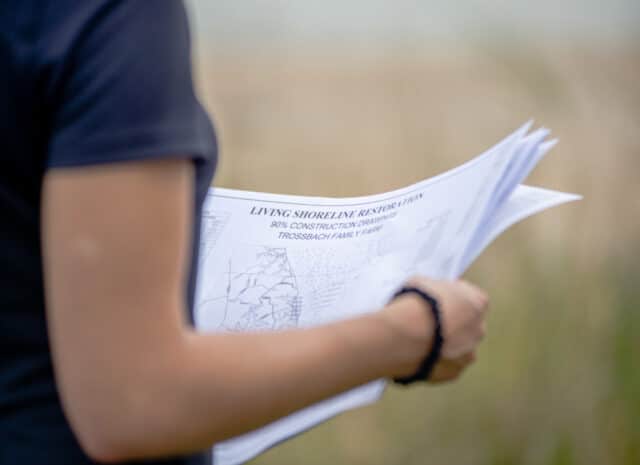 A close up of a person looing at documents entitled "Living Shoreline Restoration"