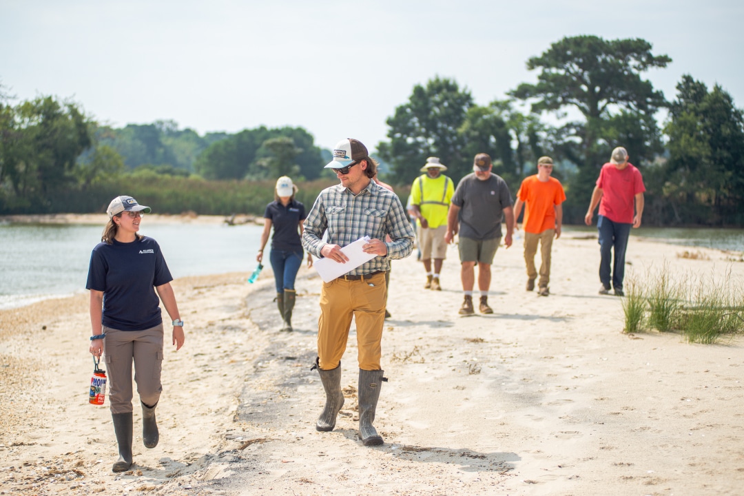 A group of people walk along a shoreline smiling and talking