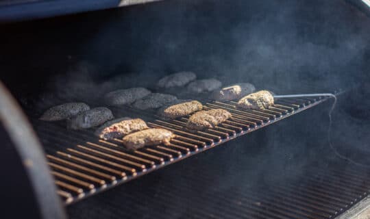 Duck breasts cook on a grill with smoke billowing