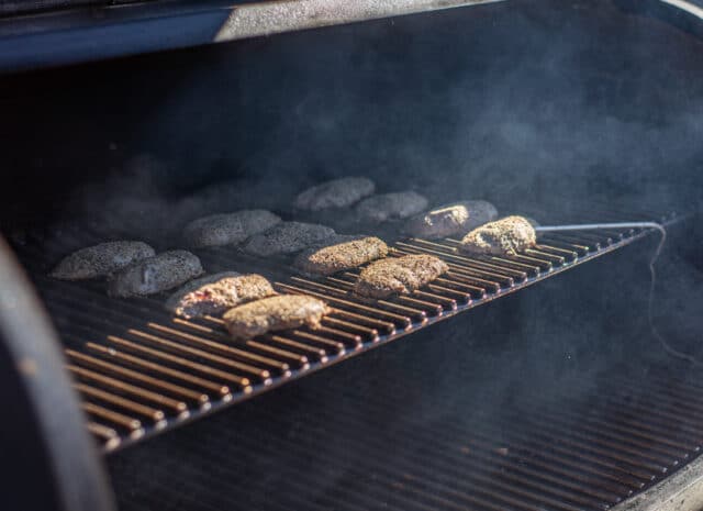 Duck breasts cook on a grill with smoke billowing