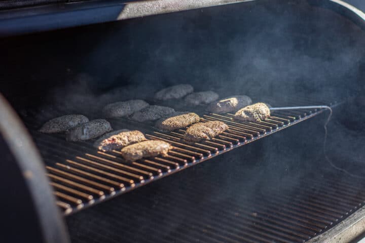 Duck breasts cook on a grill with smoke billowing