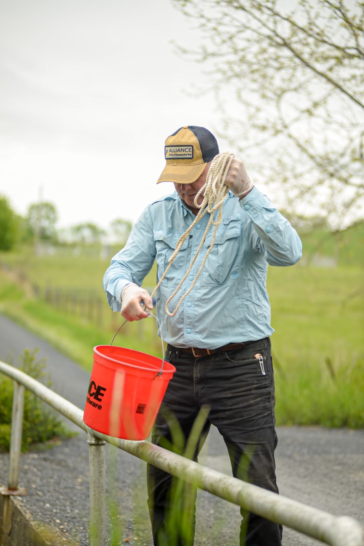 A person holding a red bucket attached to a rope on the edge of a bridge