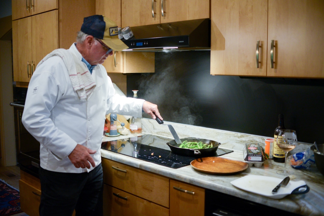 A person in a chef's coat cooks vegetables in a pan