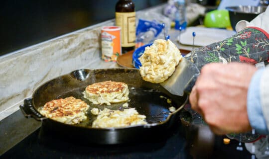 a close up of a hand flipping a crab cake in a pan