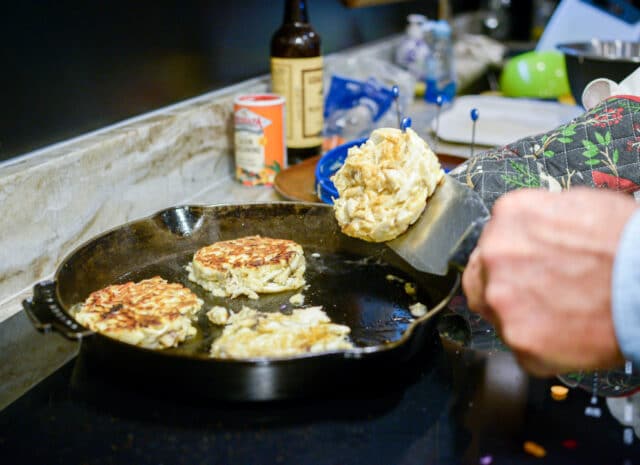 a close up of a hand flipping a crab cake in a pan