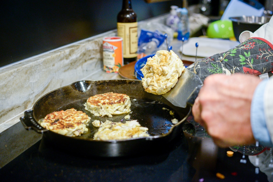 a close up of a hand flipping a crab cake in a pan