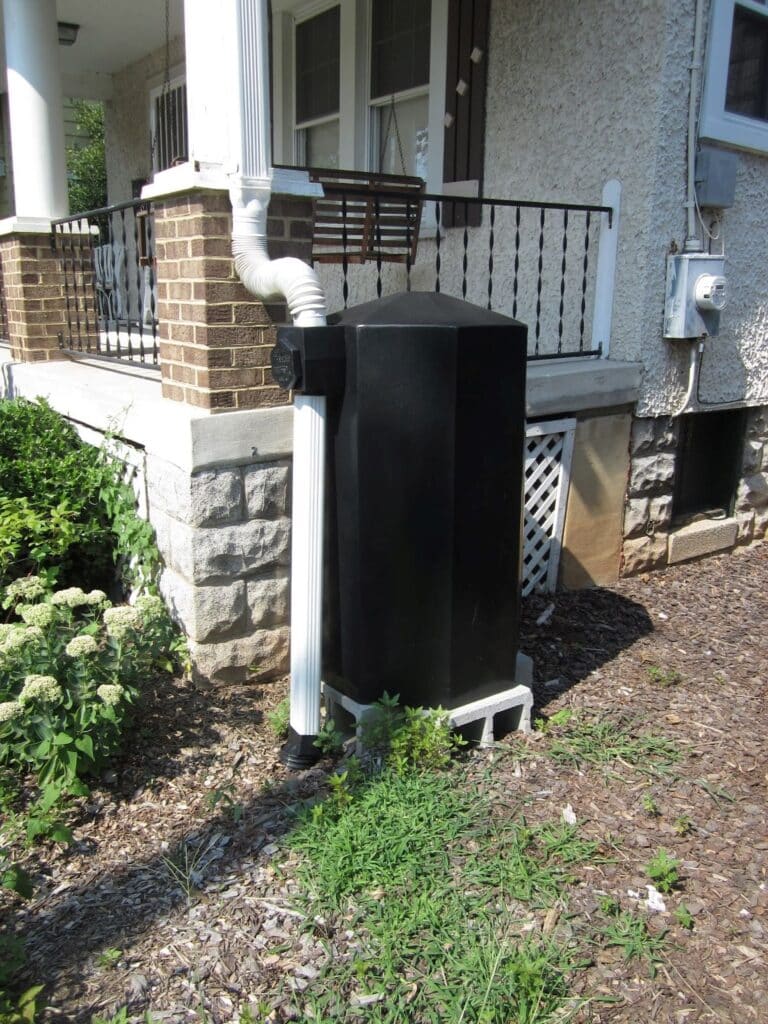 a black rain barrel connected to a downspout