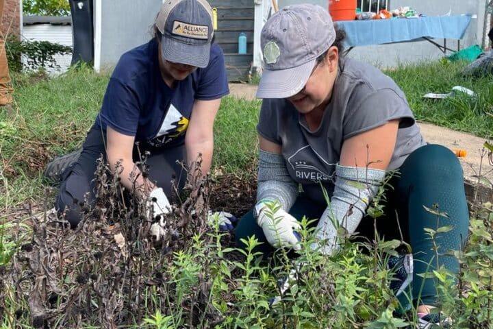 Two people smile while doing garden maintenance in a yard