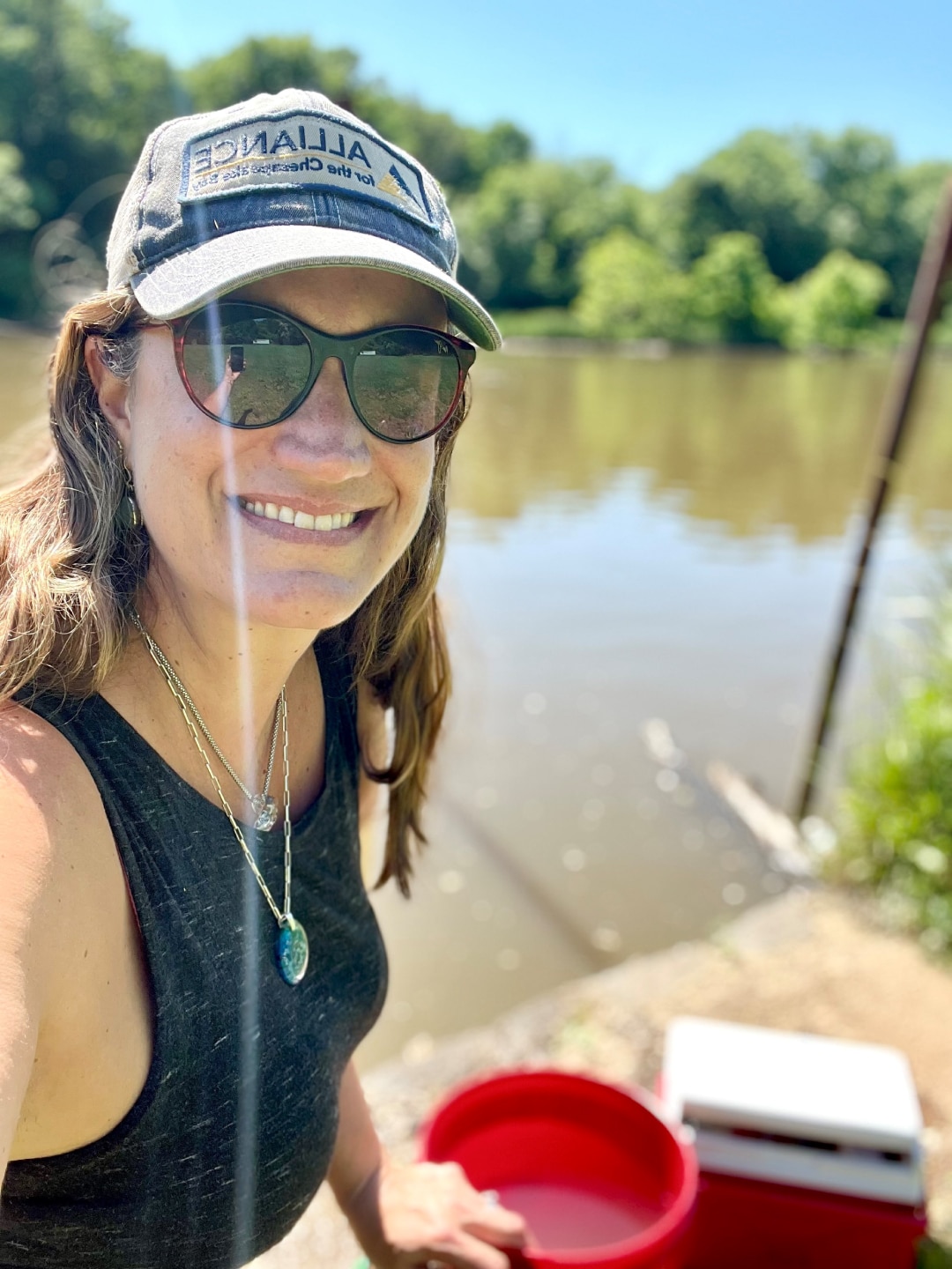 A person smiling in a selfie with a red bucket and cooler in the background