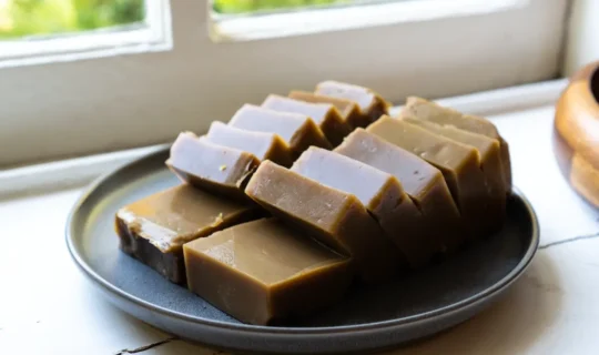 A plate of plain acorn jelly slices sitting on a plate resting on a table by a window.