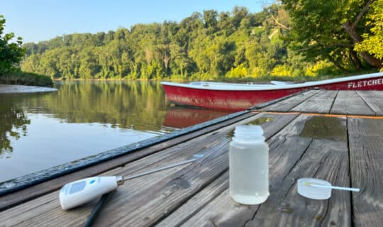 A closeup of a thermometer and water sample bottle sitting on a dock