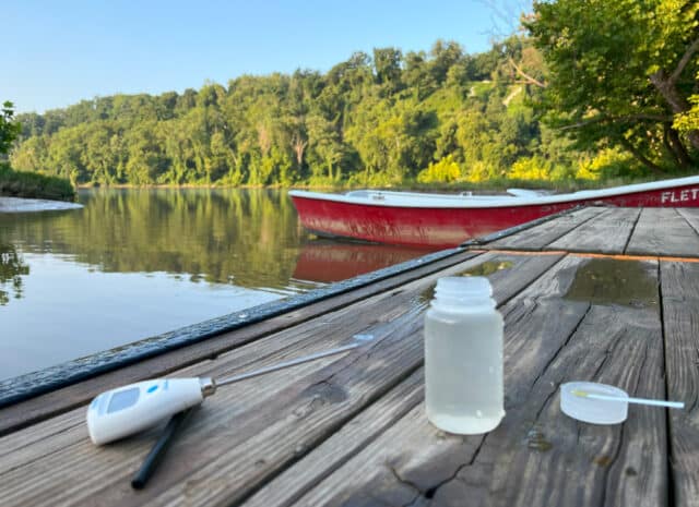 A closeup of a thermometer and water sample bottle sitting on a dock