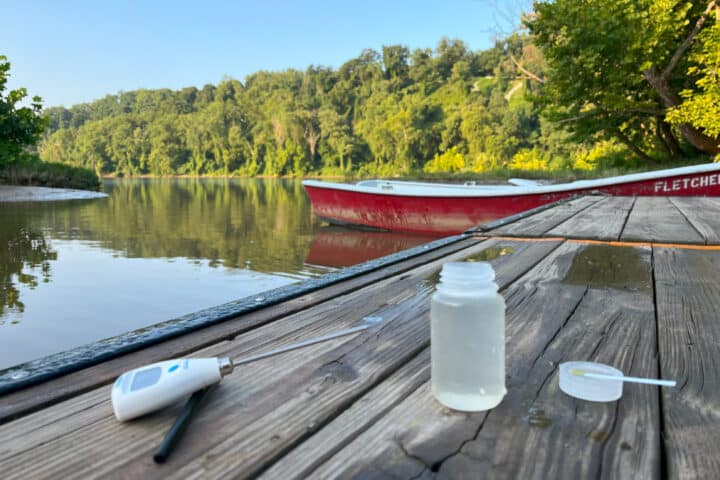 A closeup of a thermometer and water sample bottle sitting on a dock