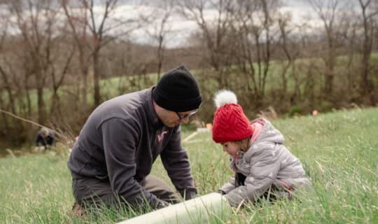 an adult and a child plant a small tree in a field