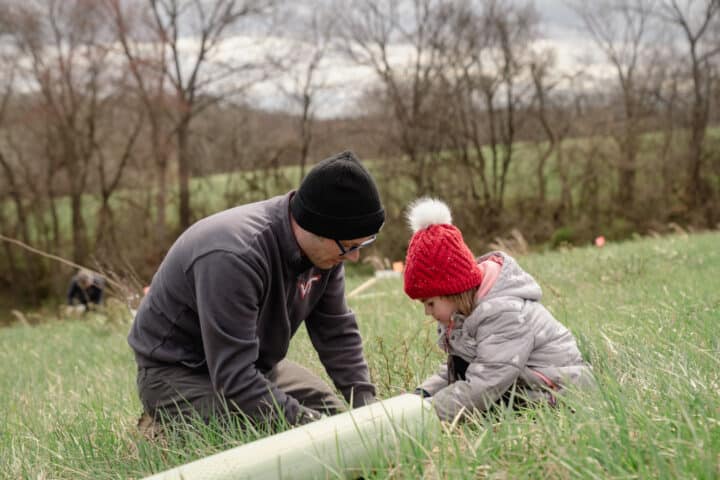 an adult and a child plant a small tree in a field